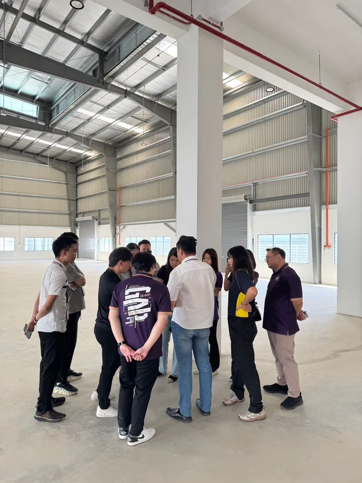 A group standing in a circle and talking inside a high-roof industrial space.