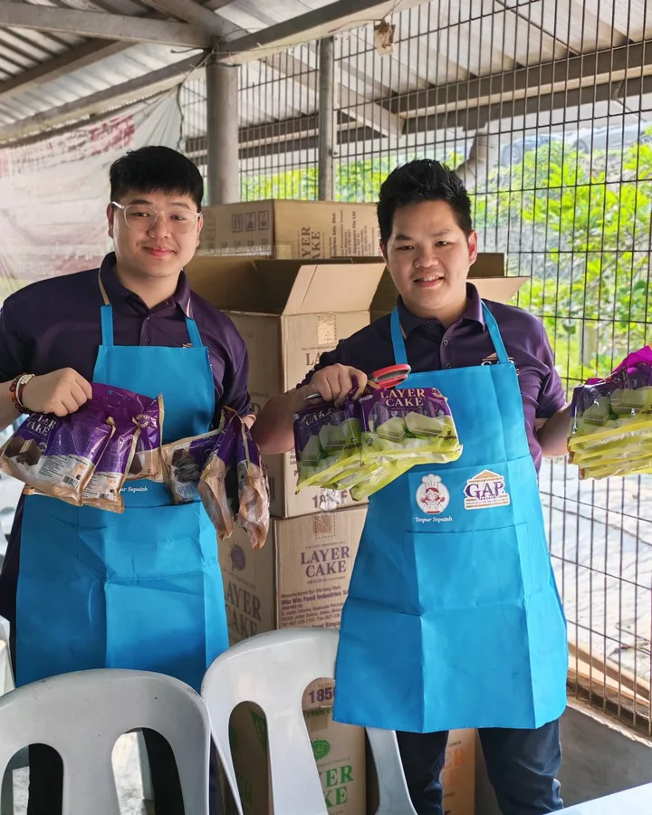 Two people in blue aprons holding packaged food beside stacked boxes.